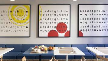 A modern dining area with a blue sofa and tables, featuring alphabet art on the walls.