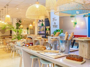 Ein Café mit Theke, auf der Brot und Gebäck ausgestellt sind, einer Kaffeemaschine und hängenden Korbtischen.