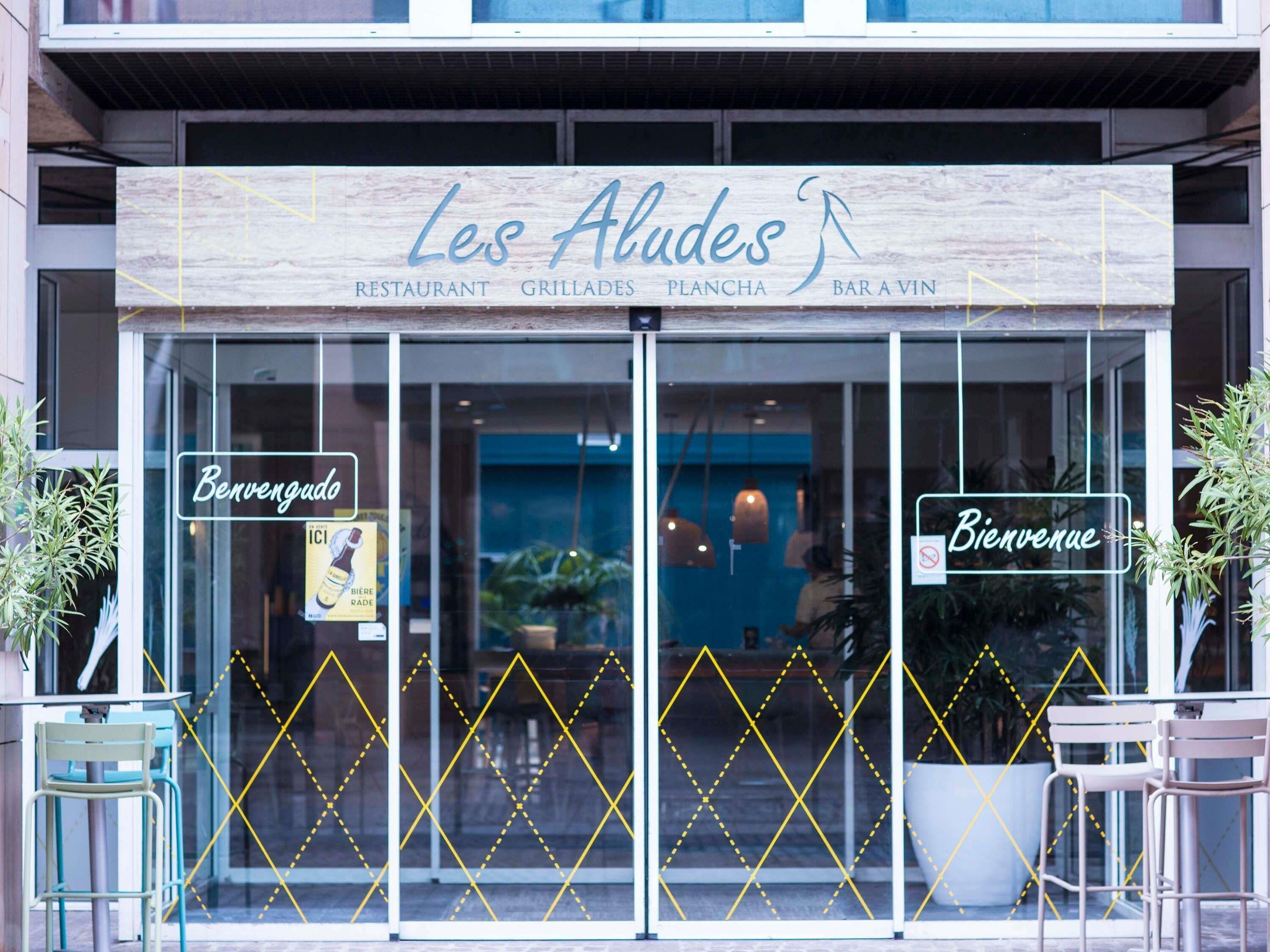 Un restaurant appelé « Les Alades », avec une enseigne, des portes vitrées et deux panneaux d’accueil.