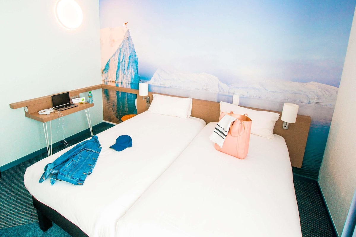 A hotel room with a bed, a desk with a laptop, and a window with a view of a snowy landscape.