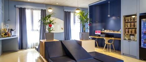A modern hotel room with a blue sofa, a desk, and a bookshelf.