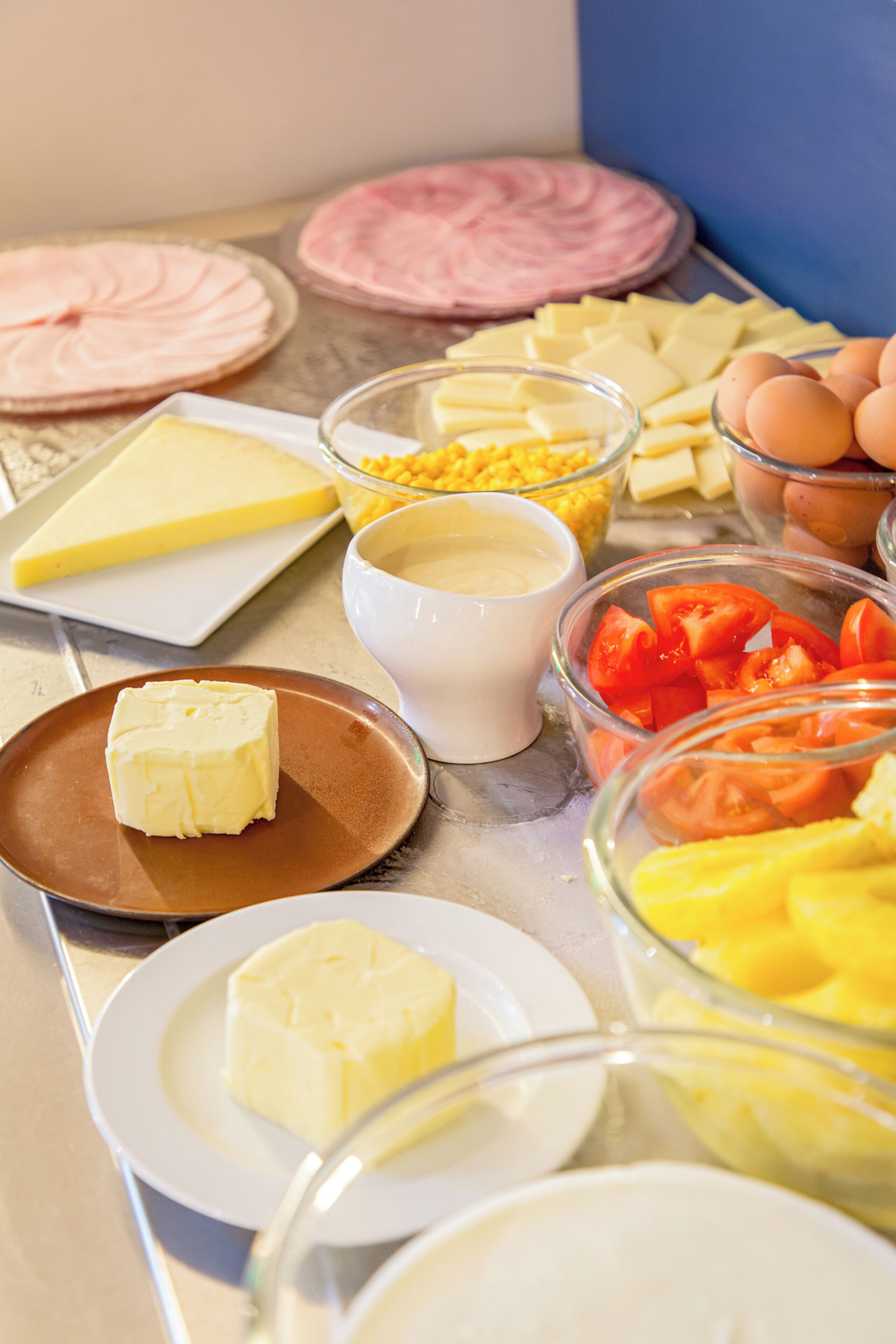 A breakfast buffet with various food items including butter, cheese, eggs, and tomatoes.