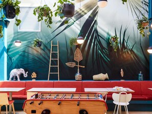 A restaurant with a wall mural, hanging plants, a wooden foosball table, and a red cushioned seating area. - ibis Styles Toulon Centre Port (Toulon)