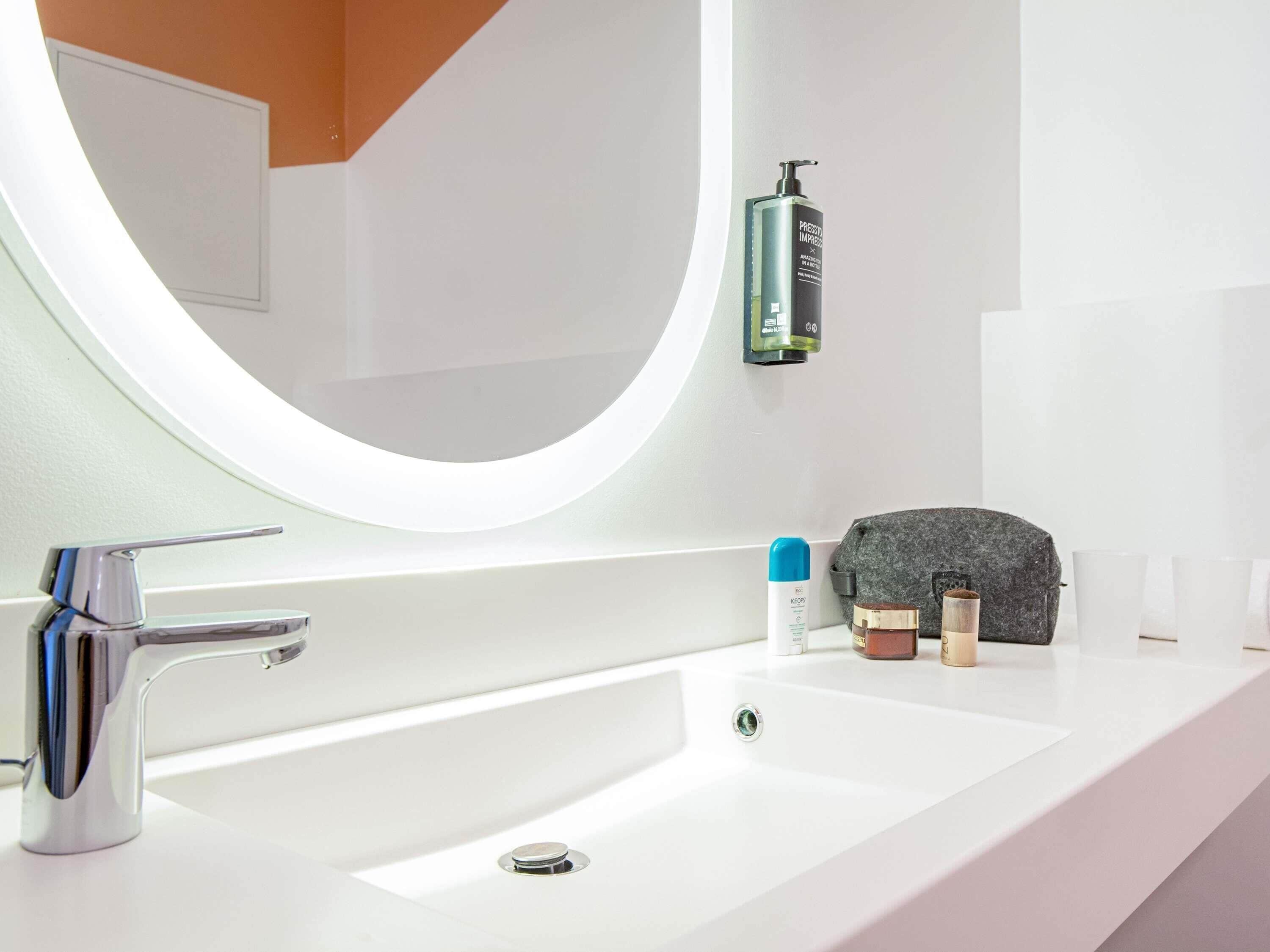 Un baño moderno con lavamanos blanco, grifo cromado y espejo redondo.