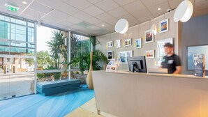 Un espace d’accueil avec un mur en verre, un comptoir de réception, un ordinateur et des tableaux encadrés accrochés au mur.