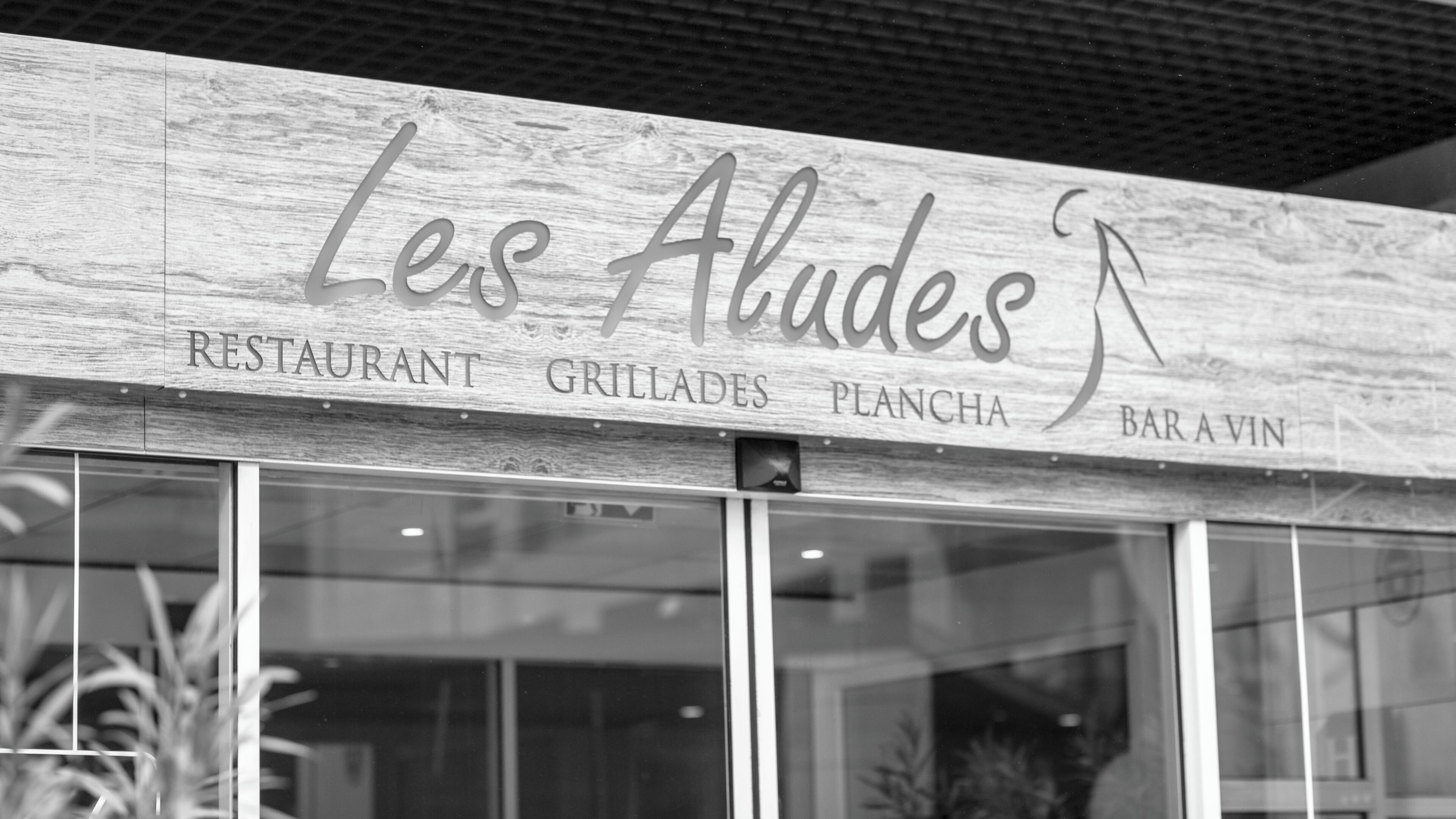 Un letrero de restaurante con el nombre 'Les Aludes' que indica 'GRILLADES', 'PLANCHA' y 'BAR AVIN'.