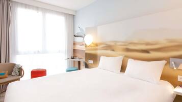 Habitación de hotel con una cama grande, un escritorio, una silla, una maleta y una ventana con cortinas.