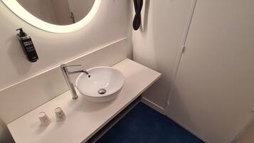 A modern bathroom with a white sink, a round mirror, a towel rack, and a hand dryer.