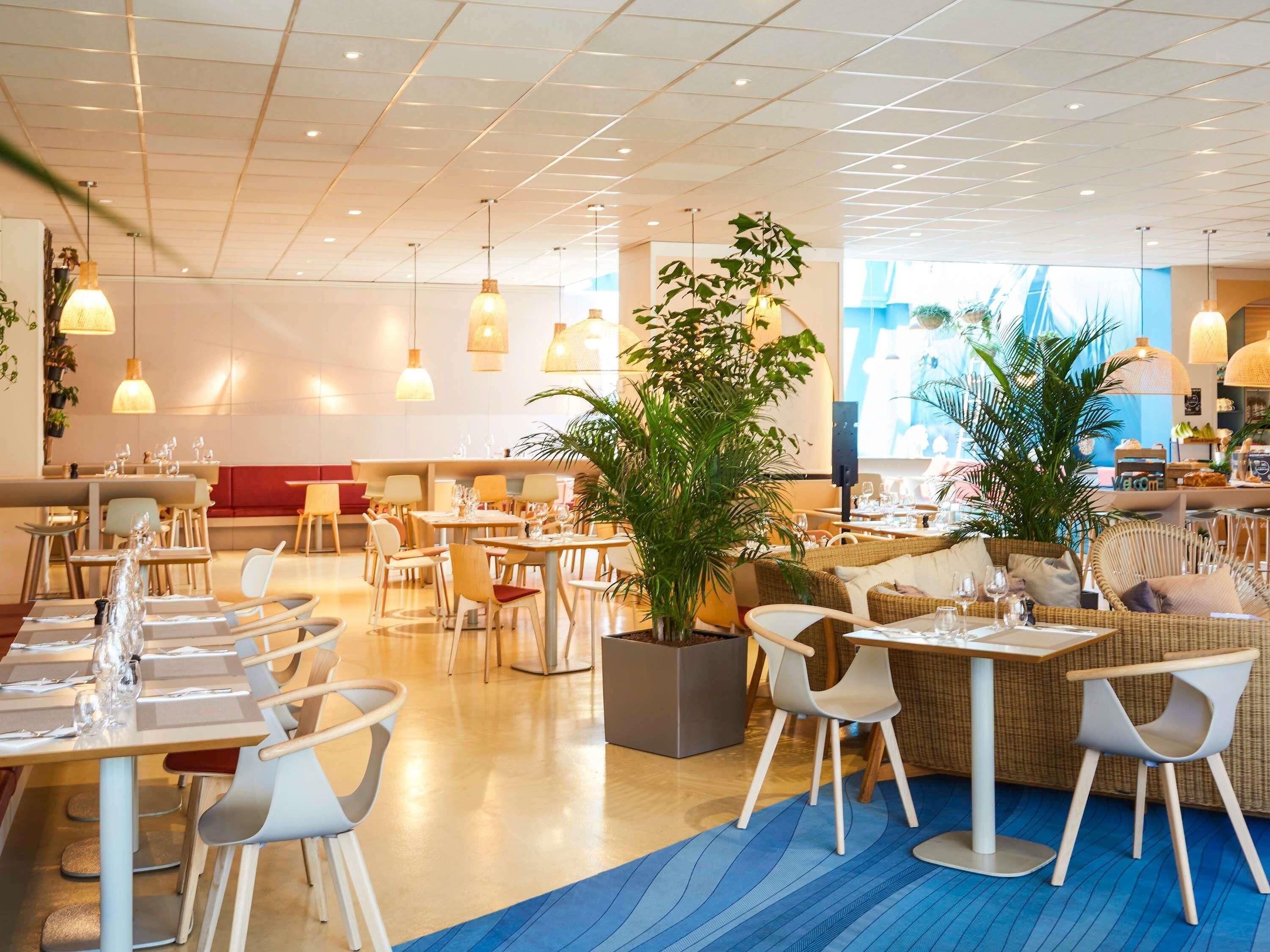 Ein modernes Restaurant mit Tischen, Stühlen, Topfpflanzen und Hängelampen.