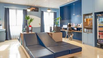 Un hall d’hôtel moderne avec un canapé bleu, un comptoir d’accueil, un poste informatique et un réfrigérateur pour les boissons.