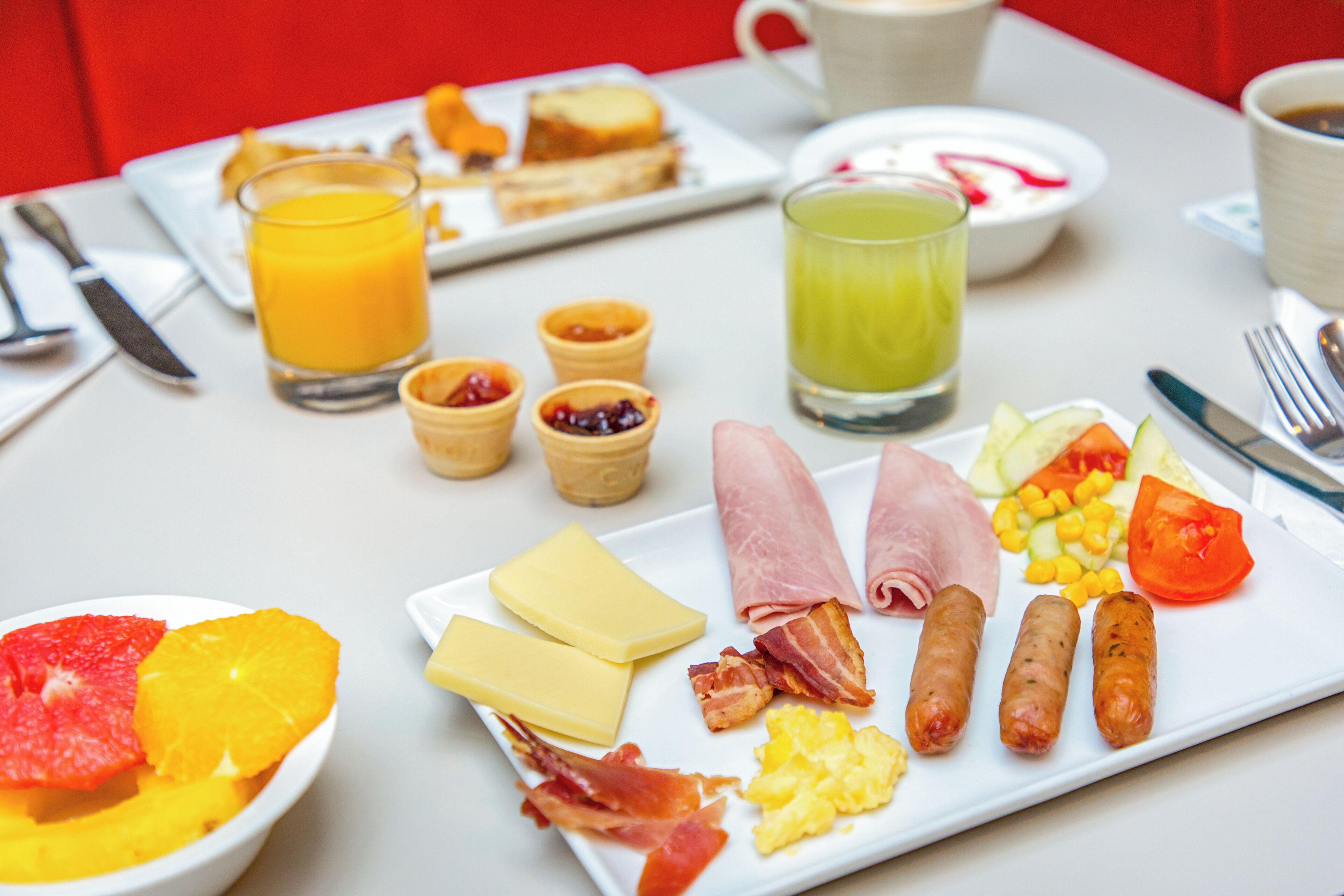 Una mesa de desayuno con platos de comida, vasos de jugo de naranja y jugo verde, y una taza de café.