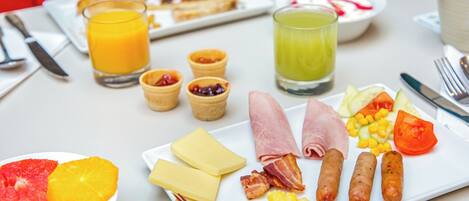 Una mesa de desayuno con platos de comida, vasos de jugo de naranja y jugo verde, y una taza de café.