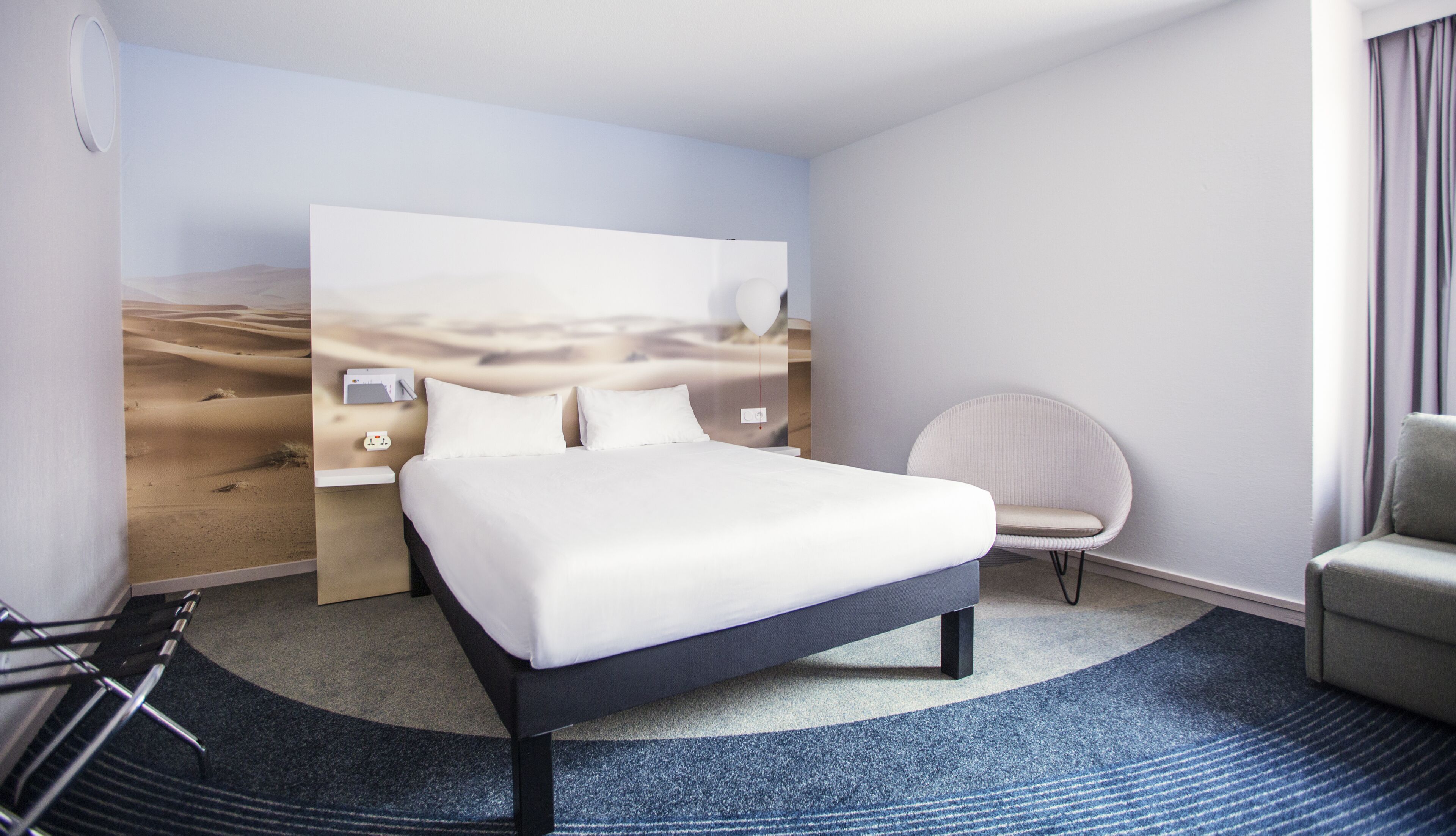 Una habitación de hotel moderna con una cama grande, un sillón redondo y un televisor montado en la pared.