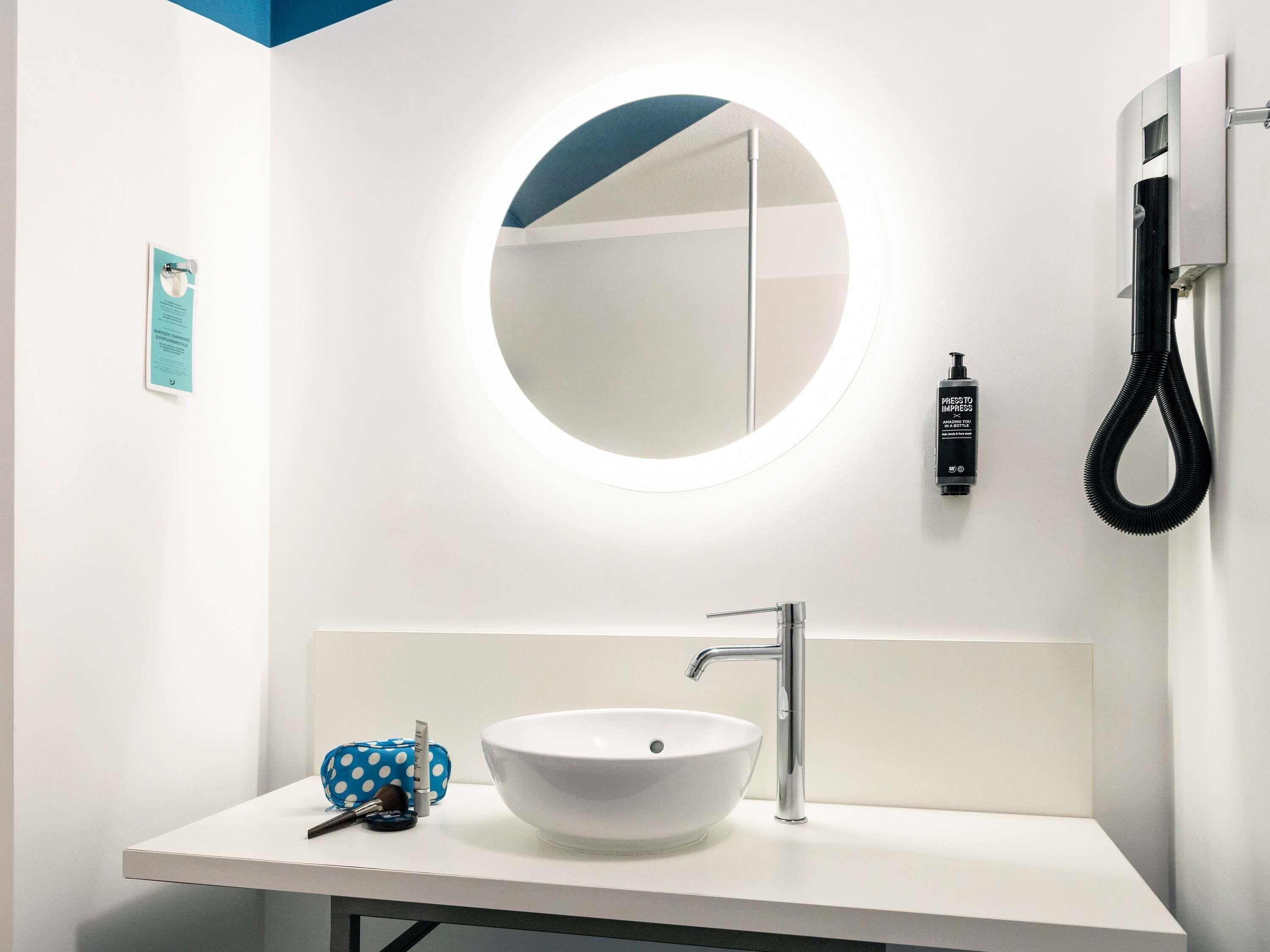 Un baño moderno con un lavabo blanco, un espejo redondo y un aspirador de mano.