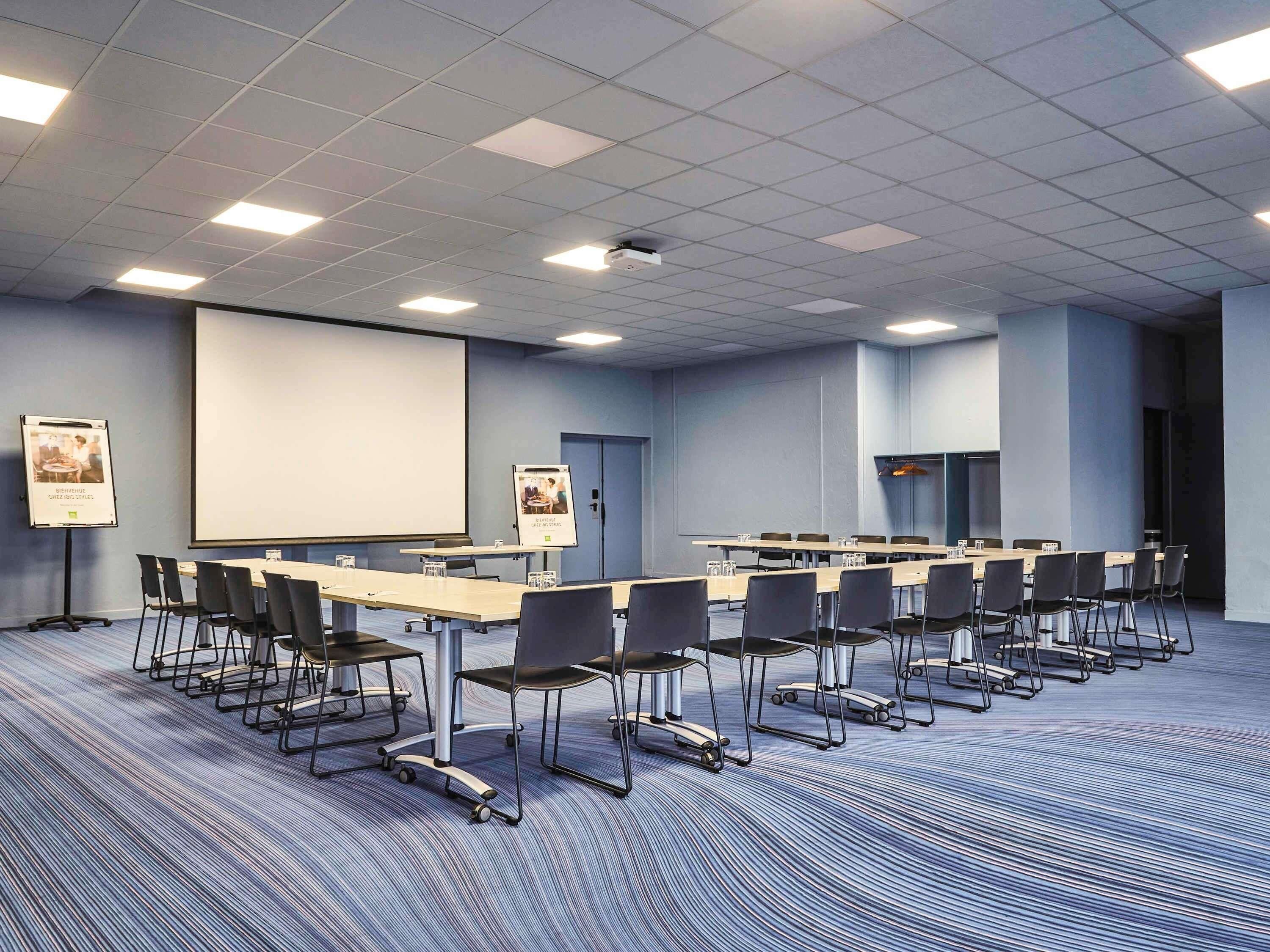 A conference room with a large screen, multiple tables, and chairs.