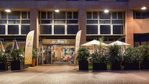 Un bâtiment abritant un restaurant appelé « Les Alouettes », situé à l’entrée, avec une terrasse dotée de parasols et de plantes en pot.