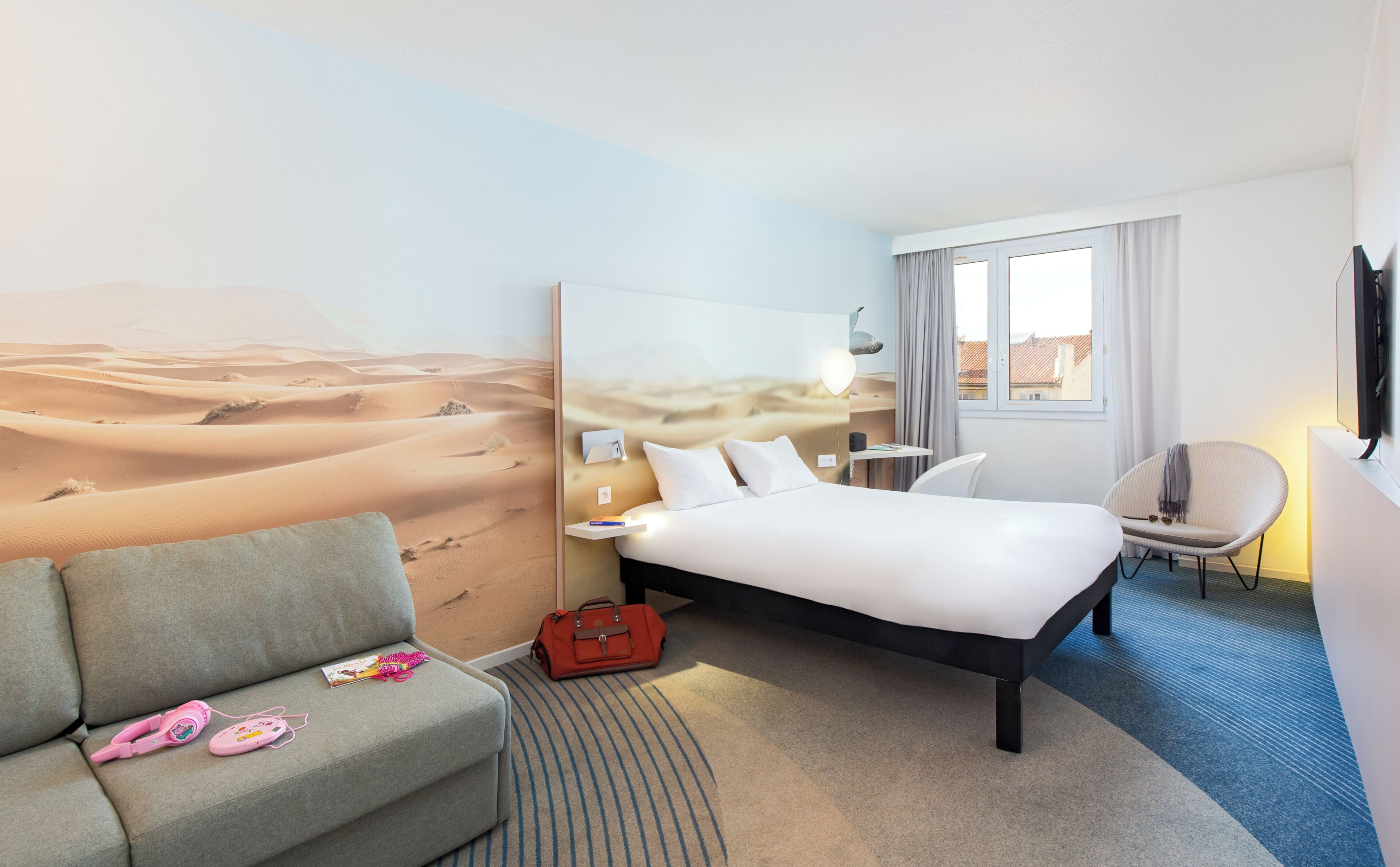 A hotel room with a bed, a sofa, a desk, a chair, and a large window.