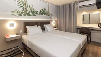 Habitación de hotel con cama, mesita de noche, lámpara, escritorio, silla y un equipo de aire acondicionado.