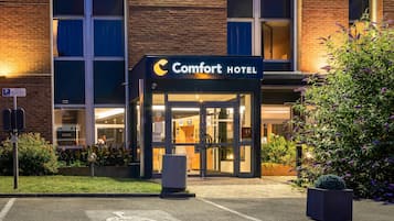 Entrada de un Comfort Hotel con puerta de vidrio, símbolo de accesibilidad para sillas de ruedas y señal de estacionamiento.