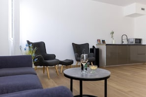A modern living room with a sofa, two armchairs, a small round table with a bottle and glass, and a kitchen area with a microwave and cabinets. - Comfort Hotel Lille L'Union (Tourcoing)