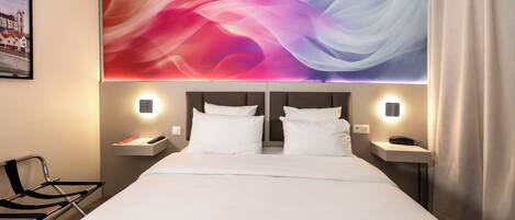 Habitación de hotel con una cama grande, dos mesitas de noche, una silla y una obra de arte colgada en la pared.