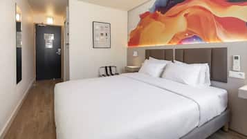 A hotel room with a large bed, a headboard, a wall-mounted artwork, a bedside table, and a door.
