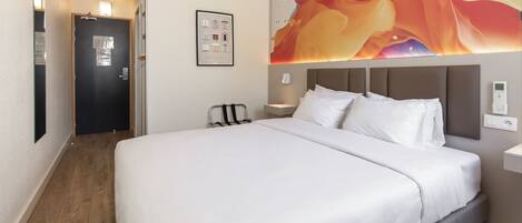 Una habitación de hotel con una cama grande, cabecera, una obra de arte en la pared, una mesita de noche y una puerta.