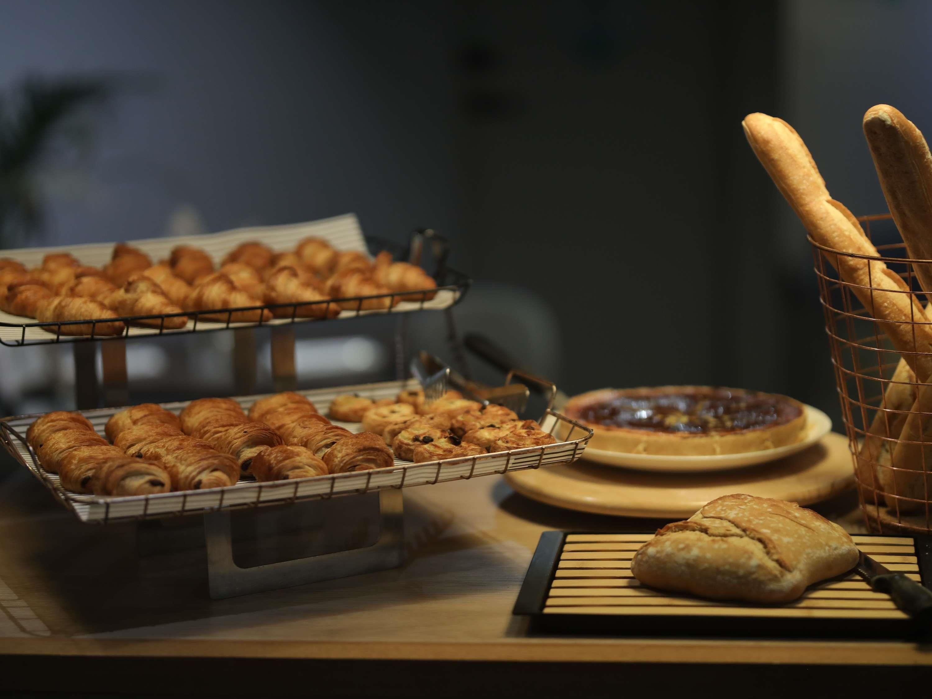 A display of baked goods including croissants and bread, arranged on trays and a wooden board.