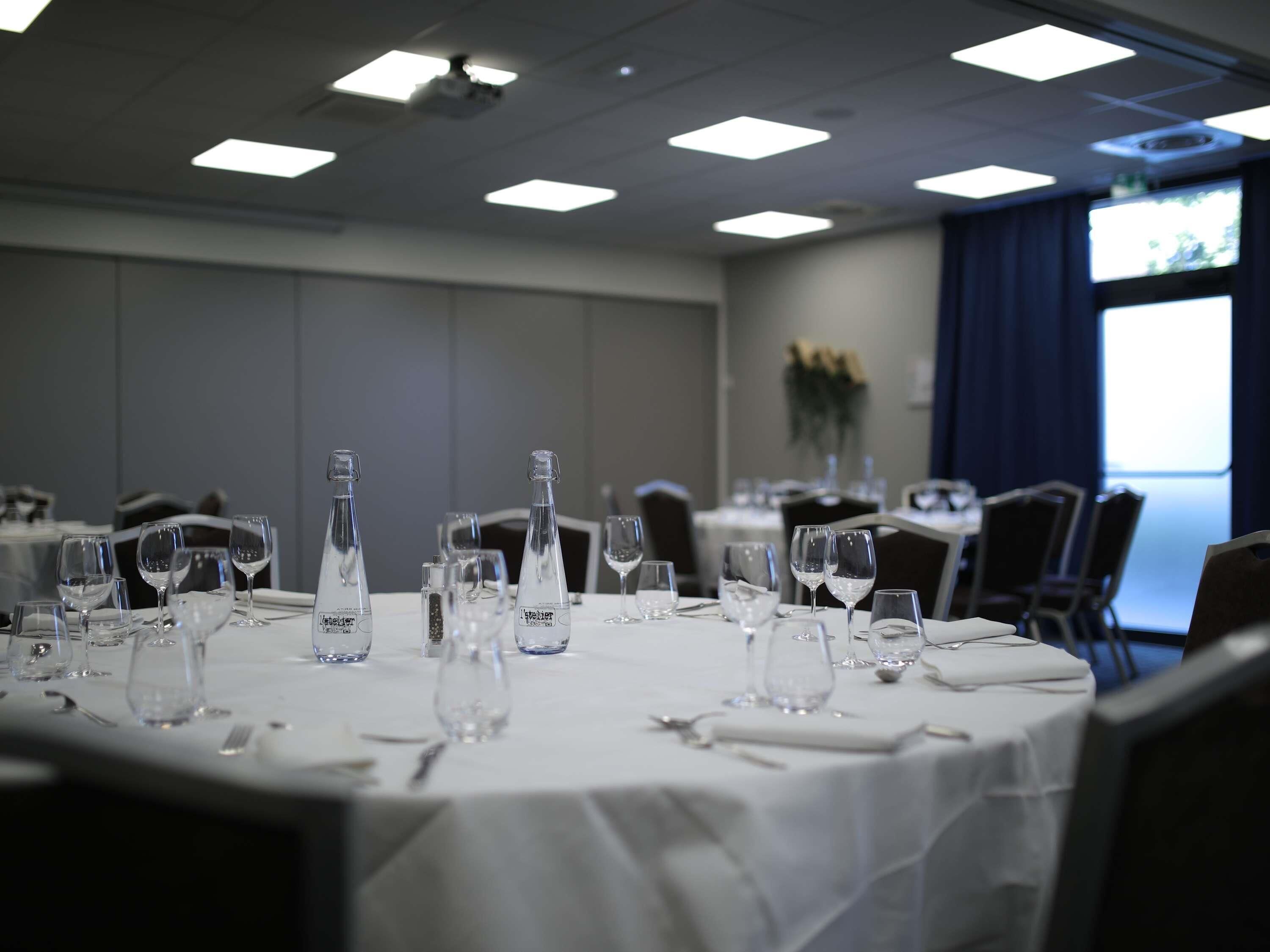 A conference room with tables set for a meeting, equipped with water bottles and wine glasses.