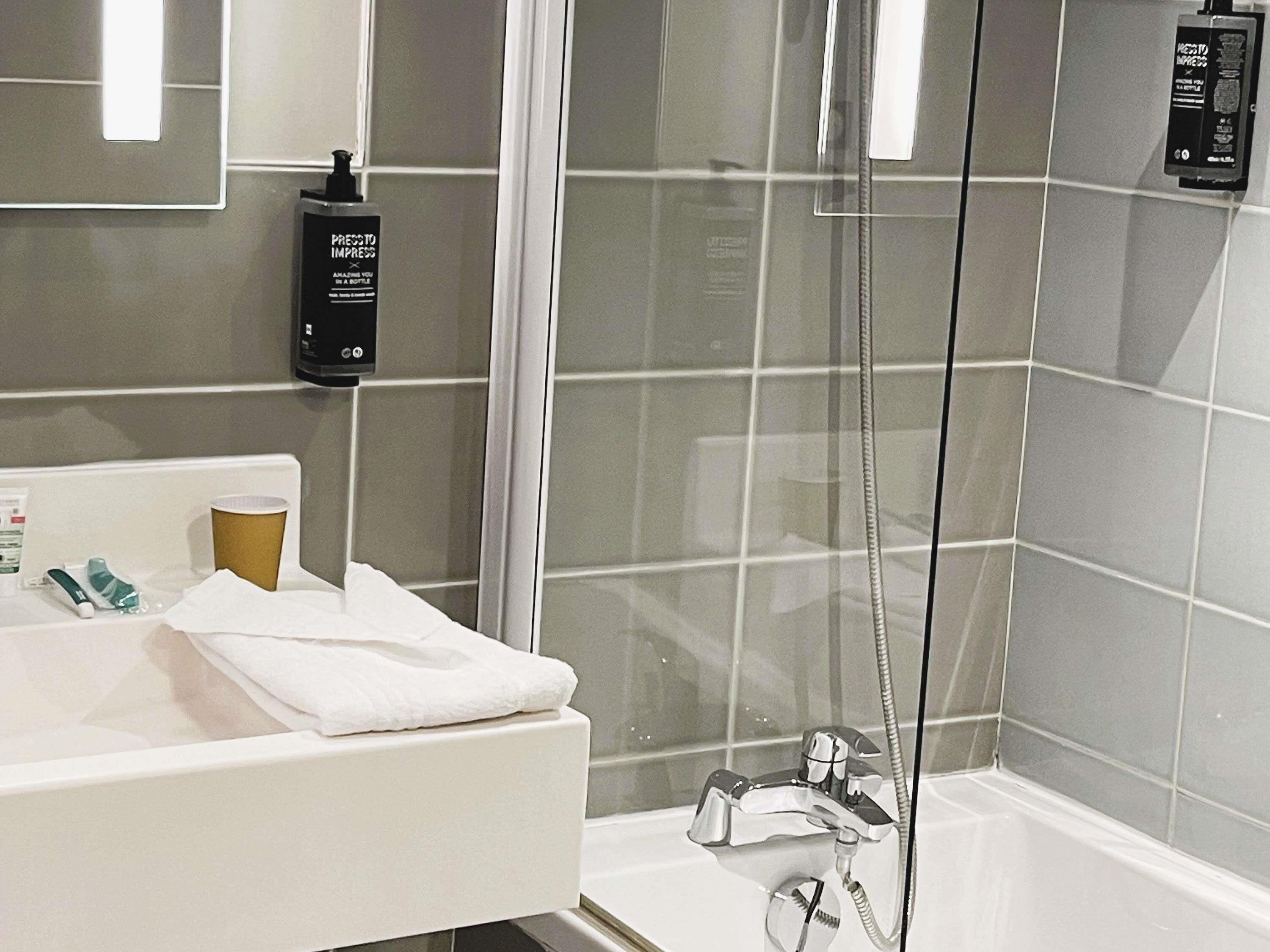 Un baño moderno con cabina de ducha de vidrio, un lavabo blanco y una botella de champú en la pared.