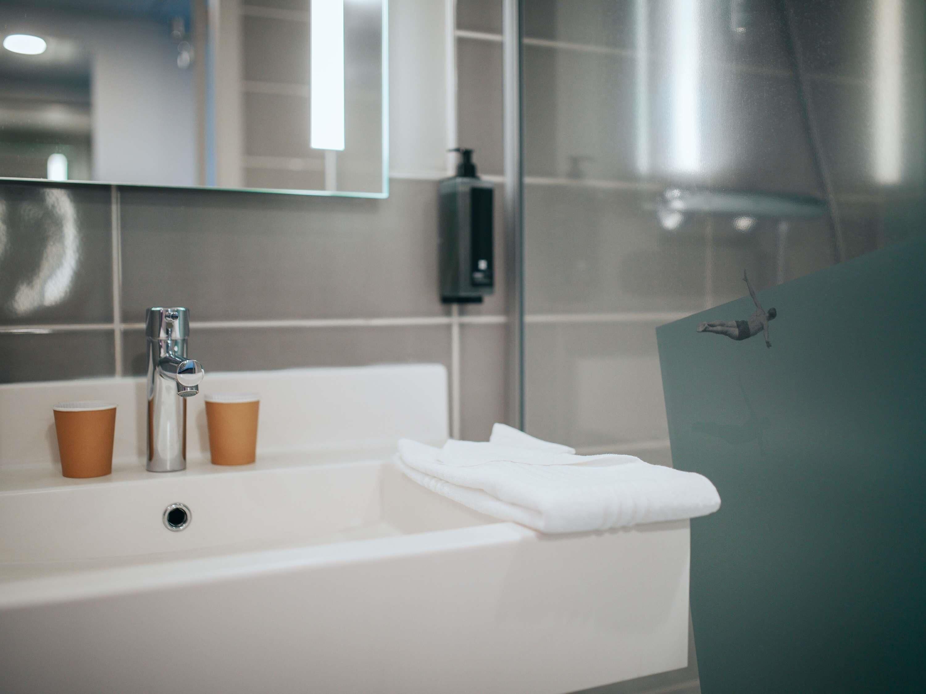 Une salle de bain moderne avec un lavabo blanc, deux tasses marron, une serviette et un miroir.
