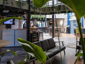 An indoor space with a counter, seating area, and hanging plants. - ibis Styles Evry Lisses (Lisses)
