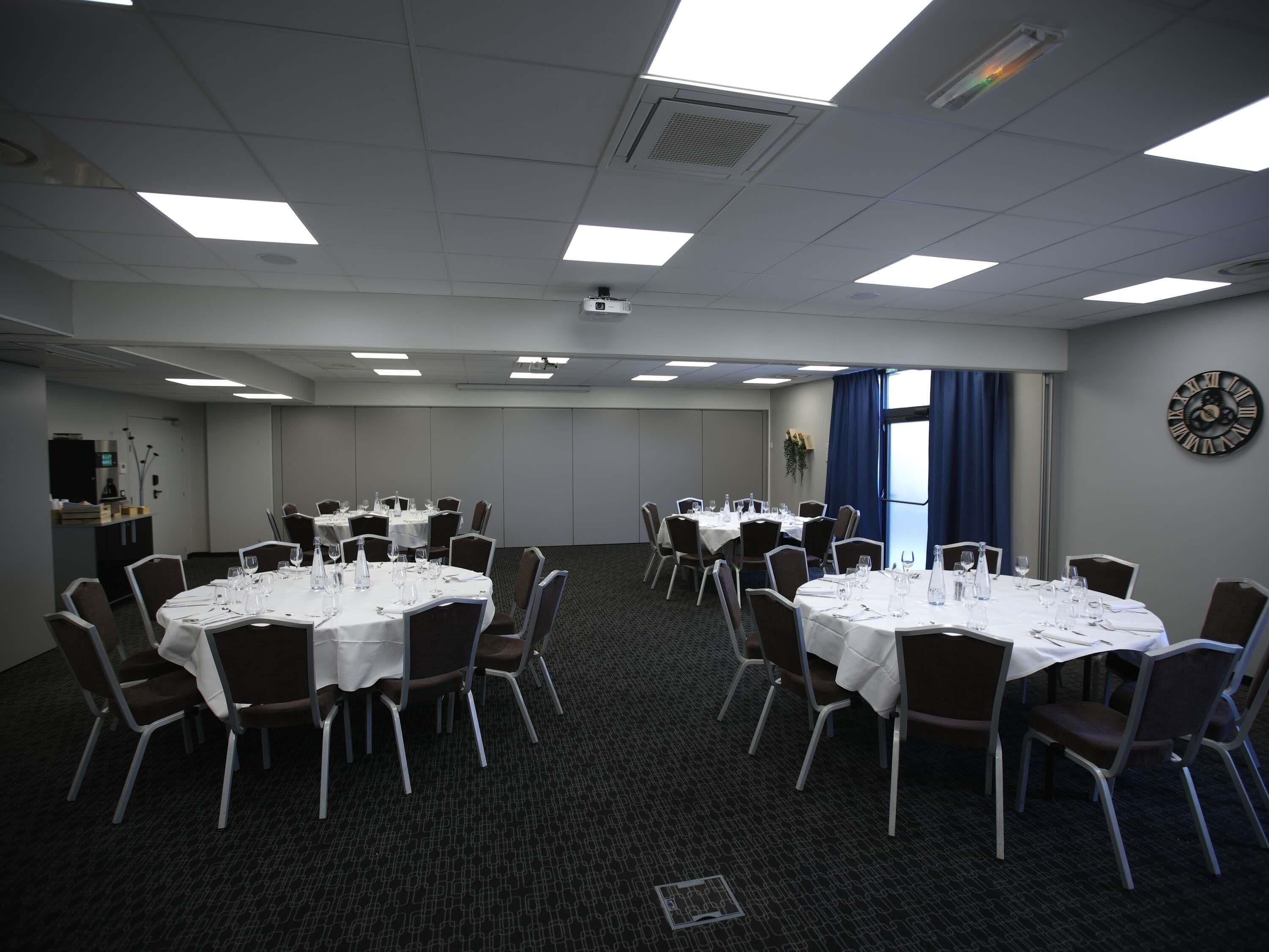 A conference room with multiple round tables, chairs, and a clock on the wall.