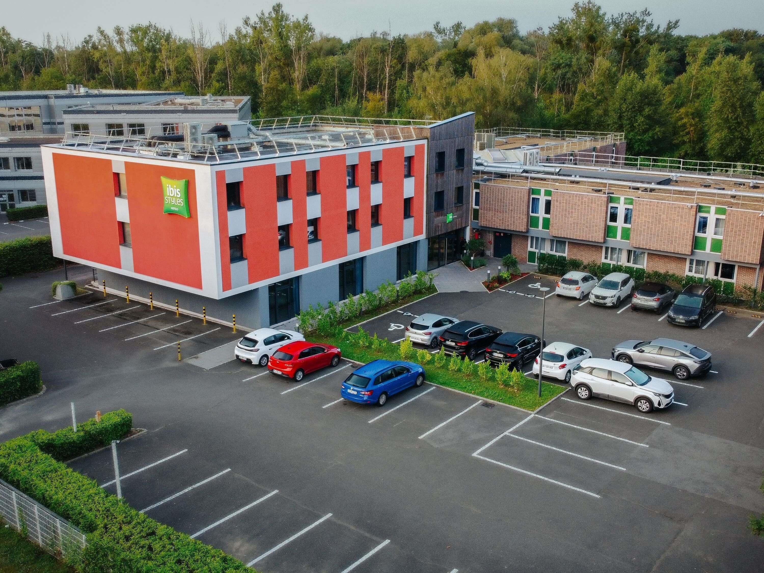A parking lot with multiple cars, a building with a red and white facade, and a green sign.