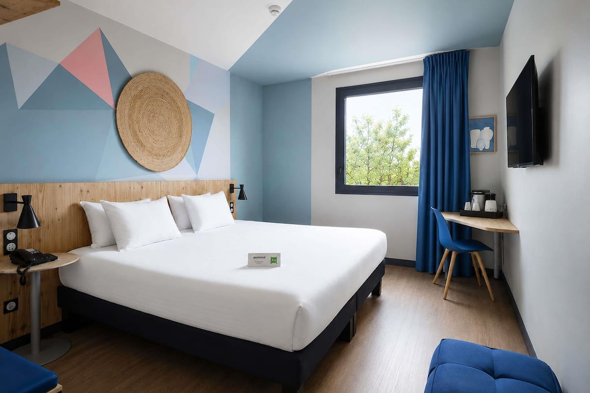 Una habitación de hotel moderna con cama, mesita de noche, lámpara y un escritorio con silla.