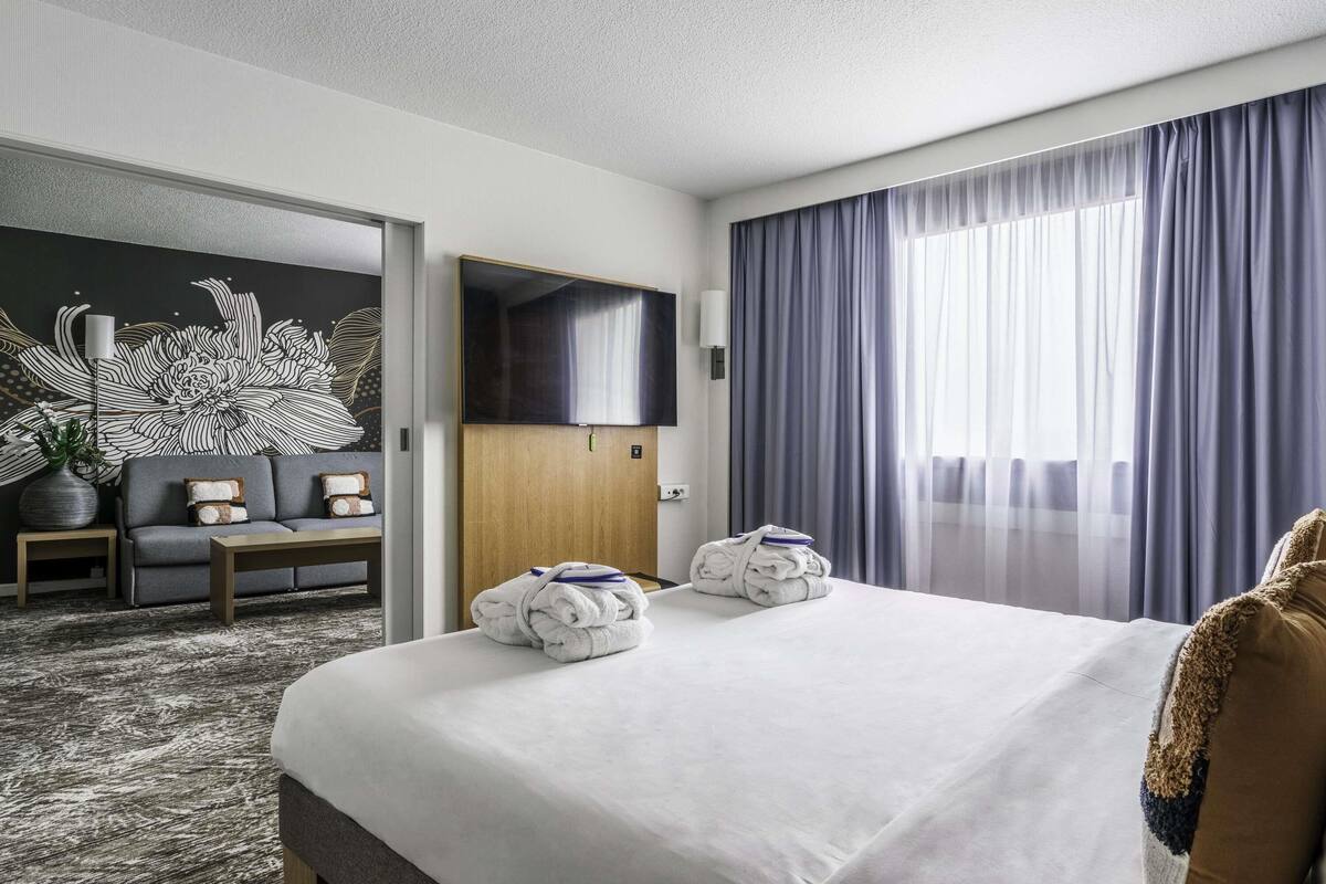 Habitación de hotel con una cama grande, un sofá, un televisor y una pared con diseño floral.
