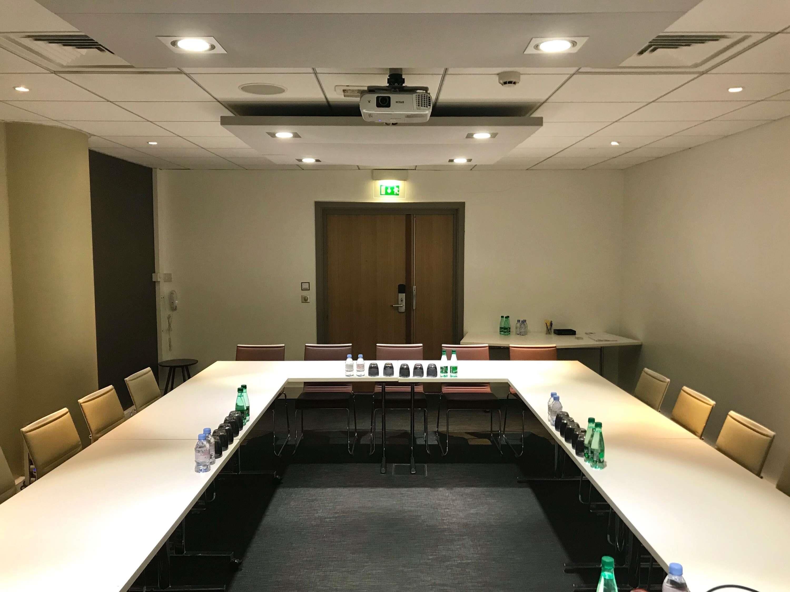 A conference room with a long table, chairs, water bottles, a projector, and an exit door.