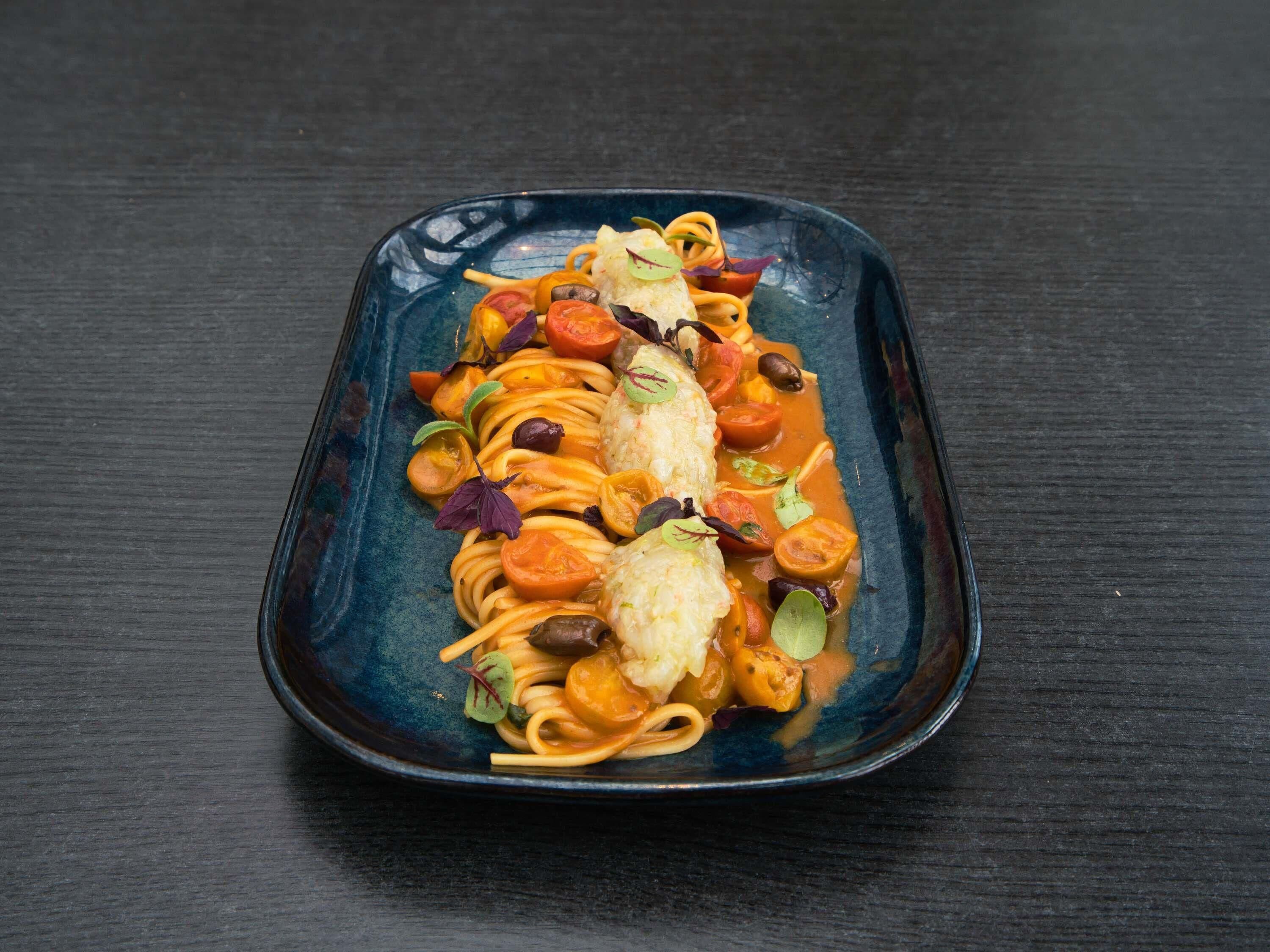 A rectangular plate with pasta and a piece of fish, garnished with vegetables and herbs.
