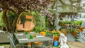 An outdoor seating area with a table, chairs, a hanging chair, and a statue. - Novotel Paris Charenton Le Pont  (Charenton-le-Pont)