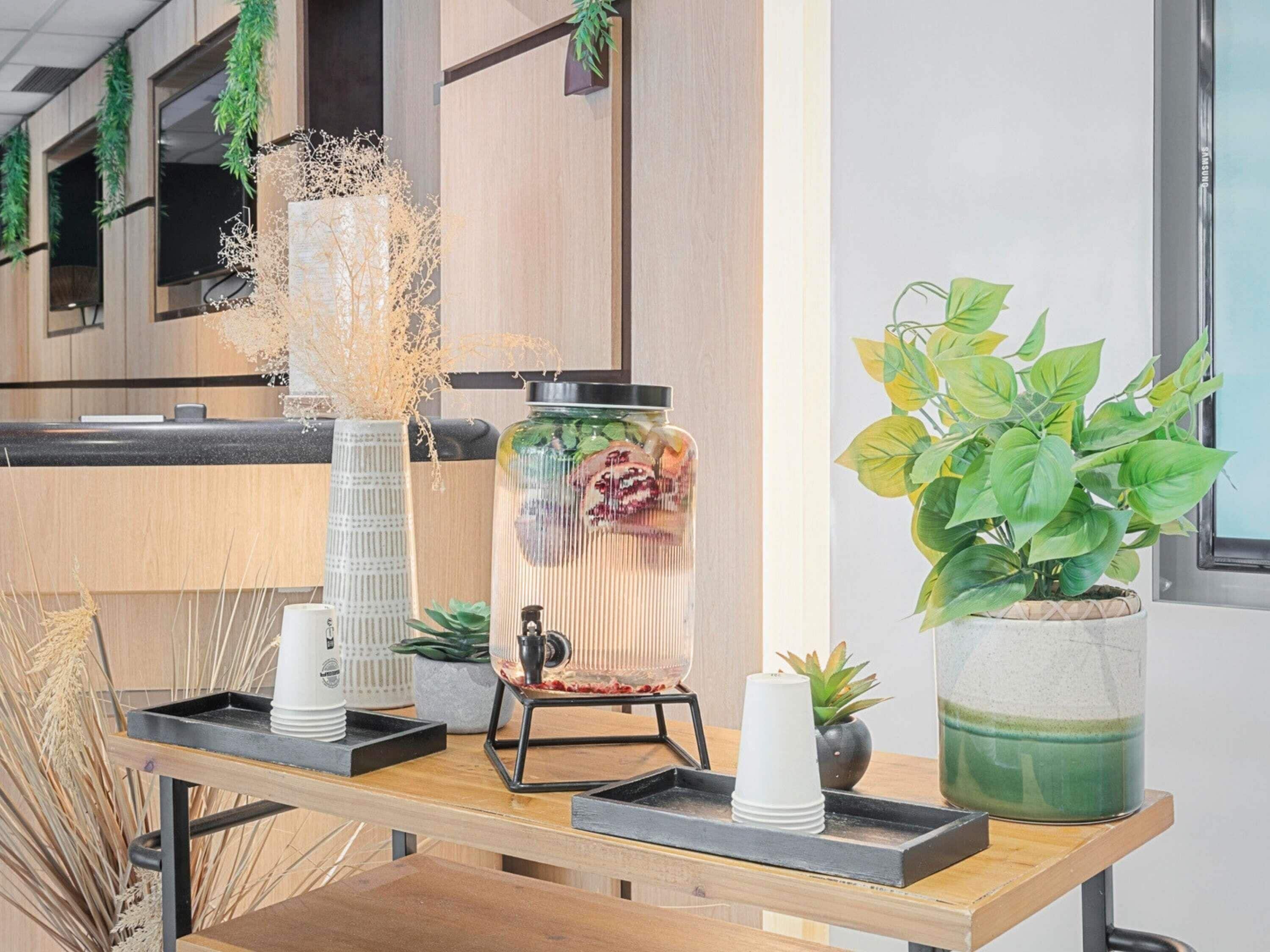 Ein Holztisch mit einer Kaffeemaschine, einem Glasbehälter mit einer Pflanze und einem Blumentopf.