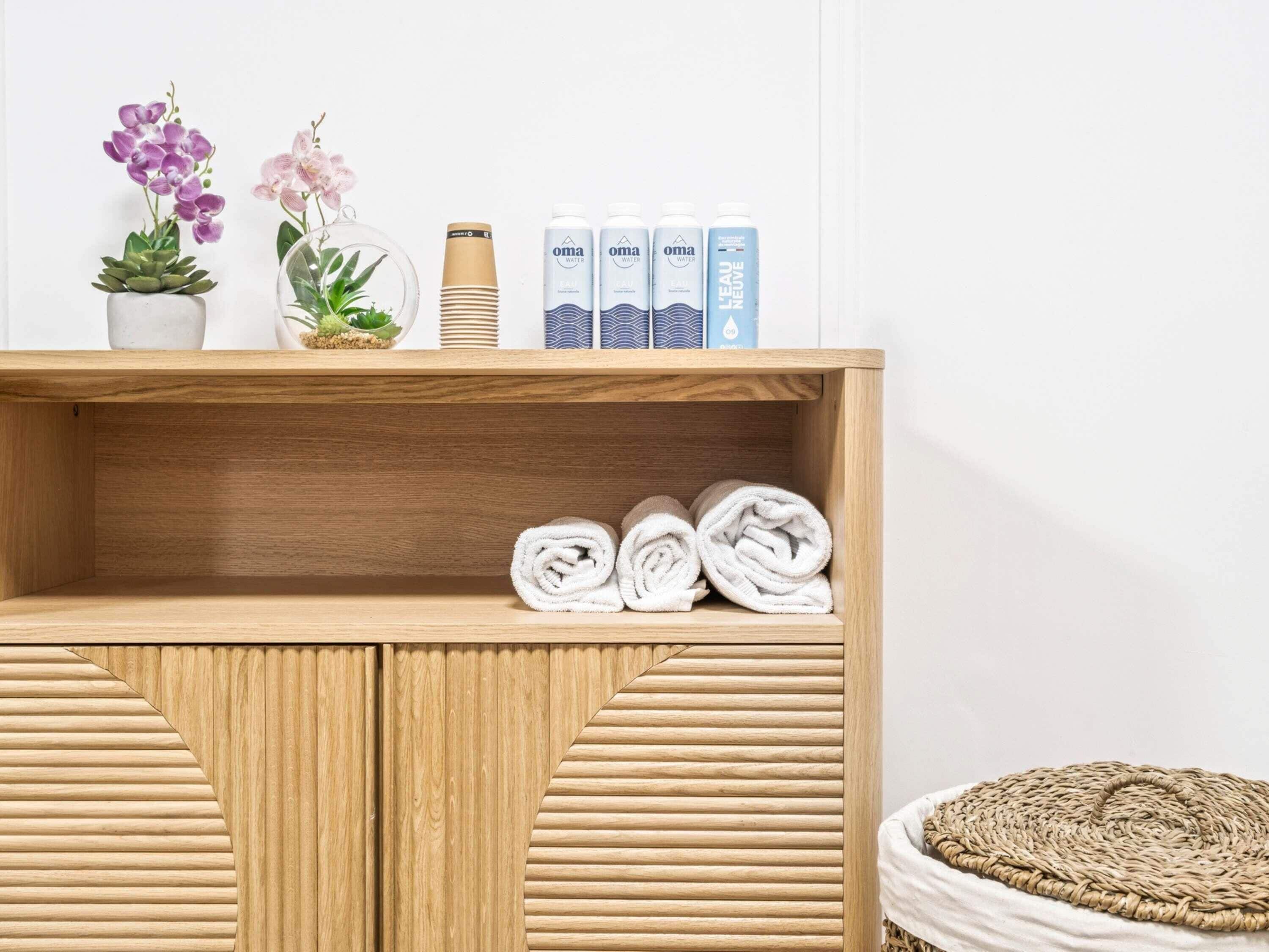 A wooden shelf with rolled towels, a potted succulent, and a glass terrarium with orchids.