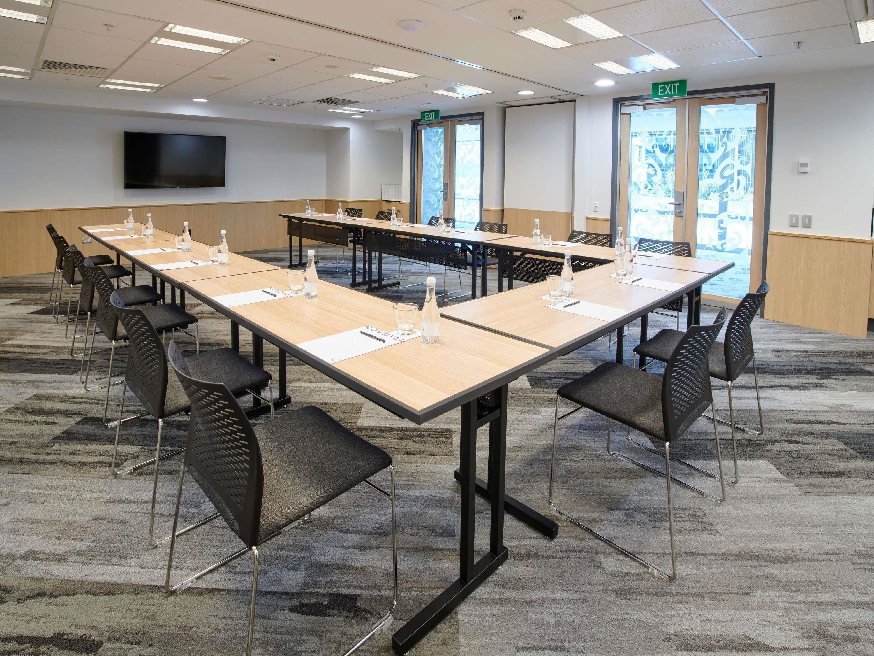 A conference room with long tables, chairs, and a flat-screen TV on the wall.