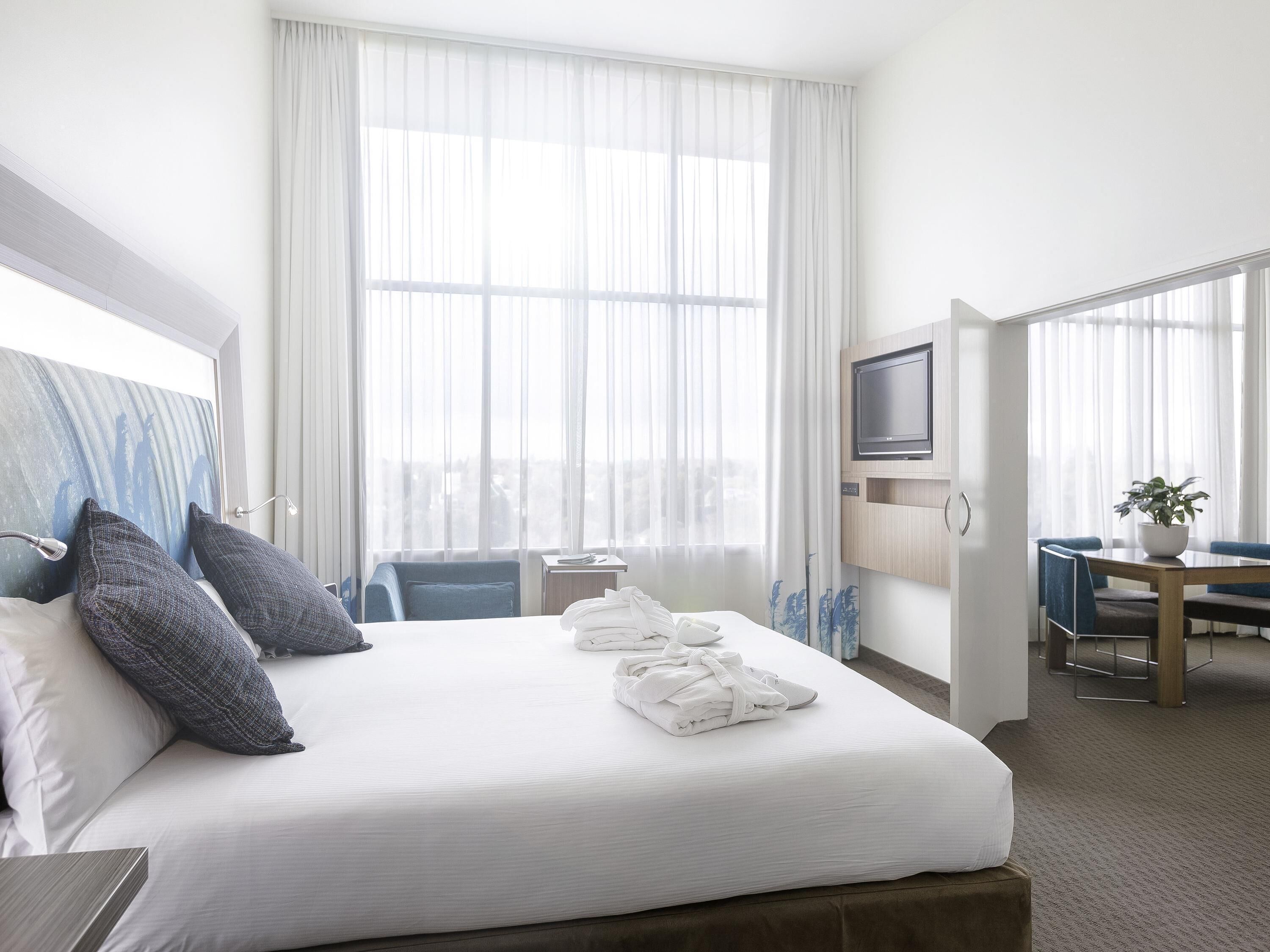 A hotel room with a bed, a desk, a television, and a view of the city.