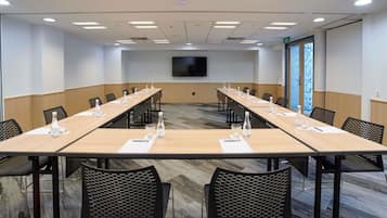 A conference room with a long table, chairs, a flat-screen TV, and a patterned carpet.