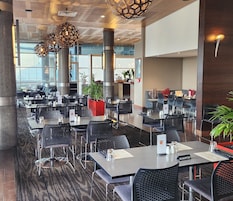 Un interior de restaurante moderno con varias mesas y sillas, ventanas amplias y lámparas decorativas.