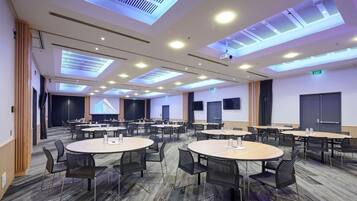 Un salón de conferencias con mesas y sillas redondas, una pantalla grande y un techo con tragaluces.