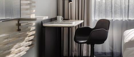 A hotel room with a modern design, featuring a desk with a lamp, a chair, and a bed.