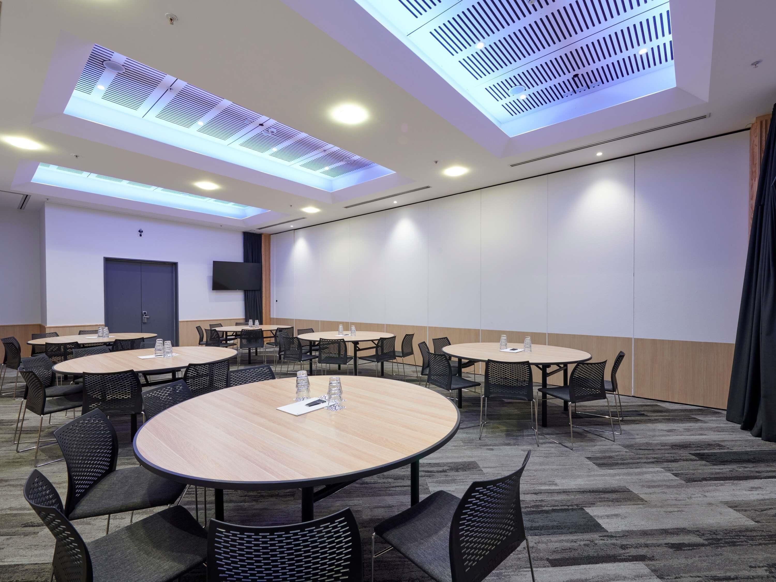 A conference room with round tables and chairs, a flat-screen TV, and a door.