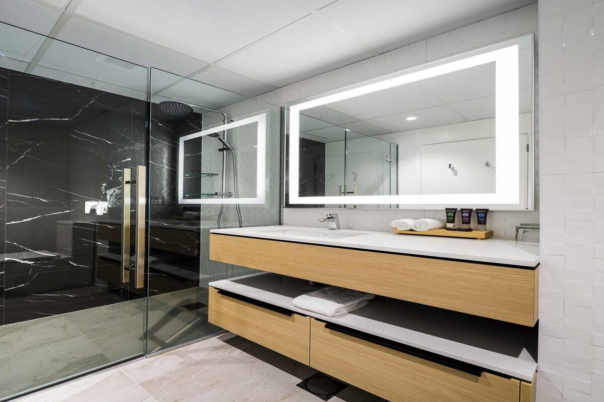 A modern bathroom with a glass shower enclosure, a white vanity with a marble backsplash, and a large mirror.