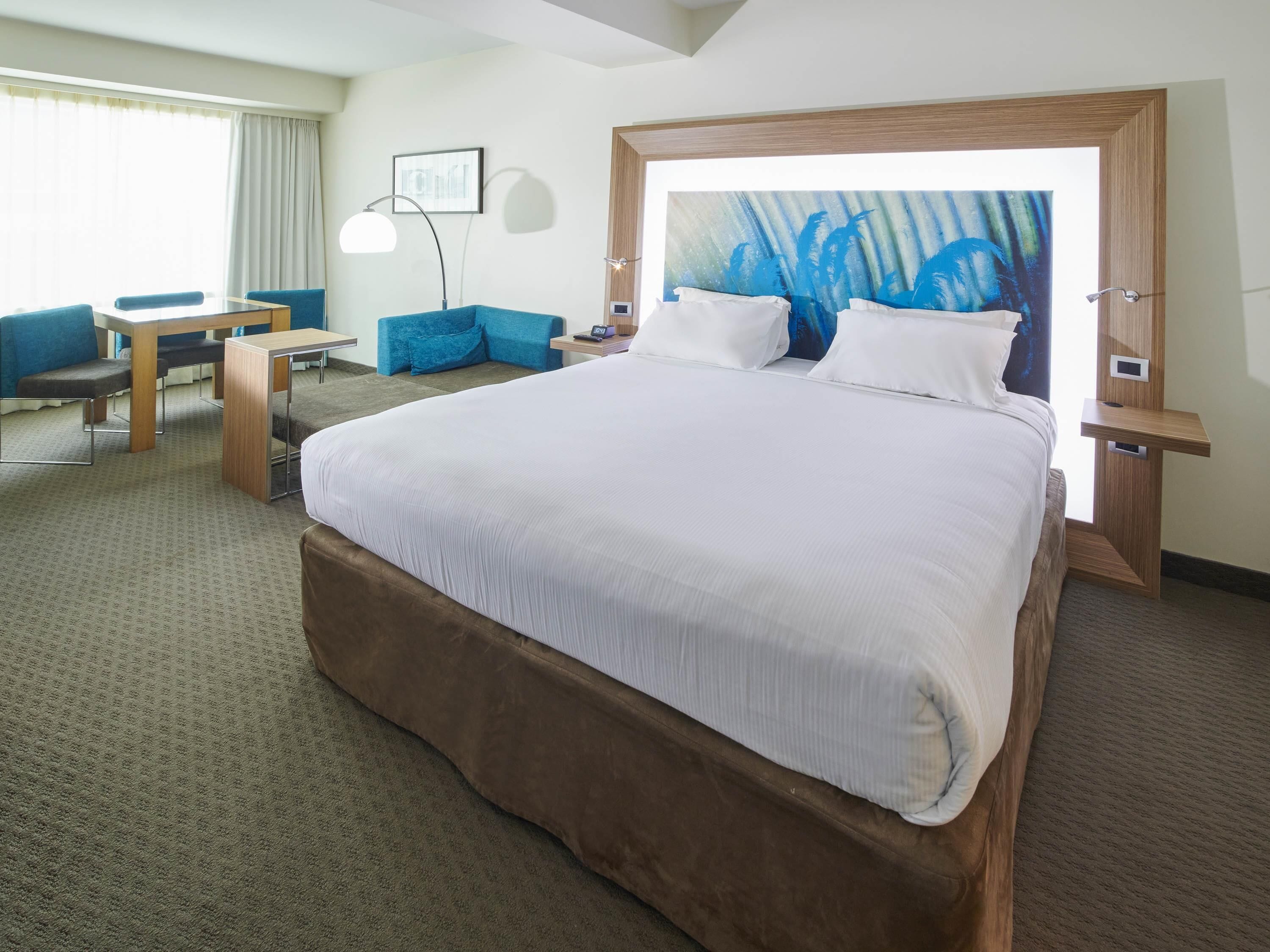 Habitación de hotel con una cama grande, un escritorio, una silla, una lámpara y un cuadro en la pared.